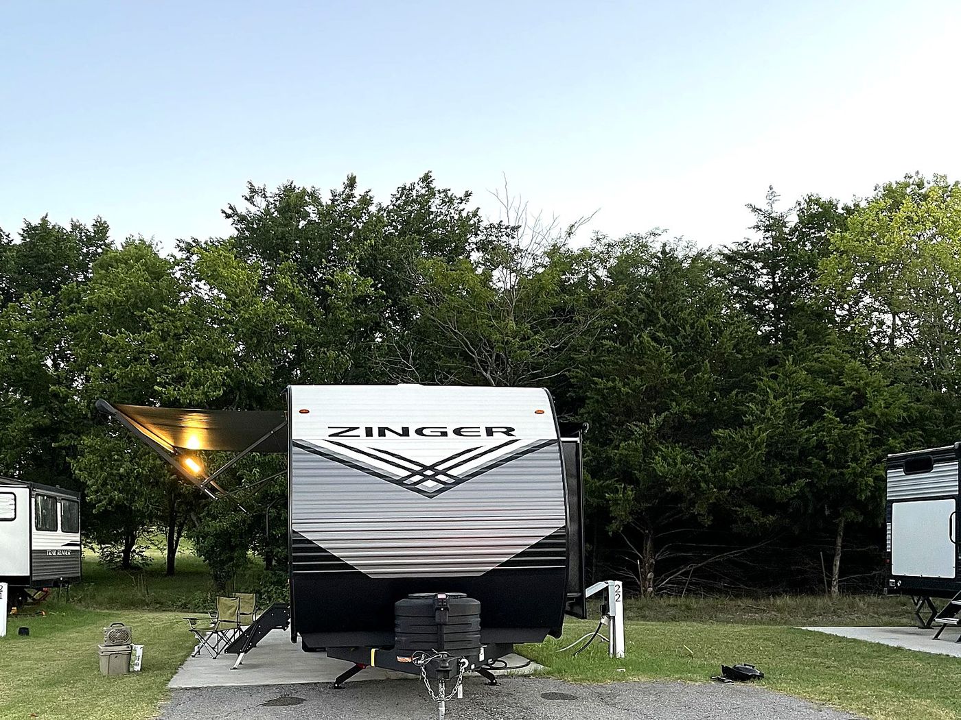 Travel trailer on an open site at dusk with the awning out and the light on